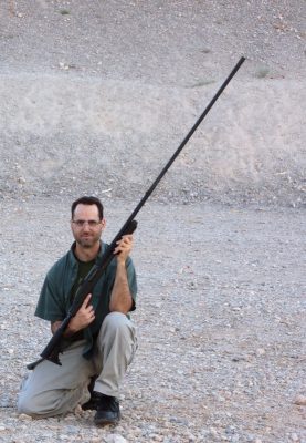 Gabriel Raviv kneeling in the desert holding a long-barreled firearm